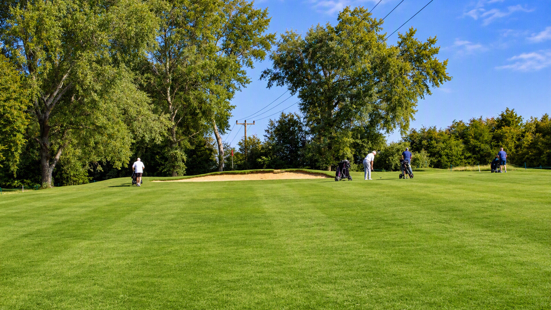Golfers with their bags on a grassy course with a sand bunker.