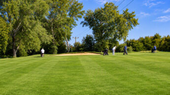 Golfers with their bags on a grassy course with a sand bunker.