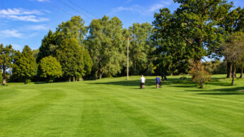 Two people walking with golf carts on a grassy golf course.