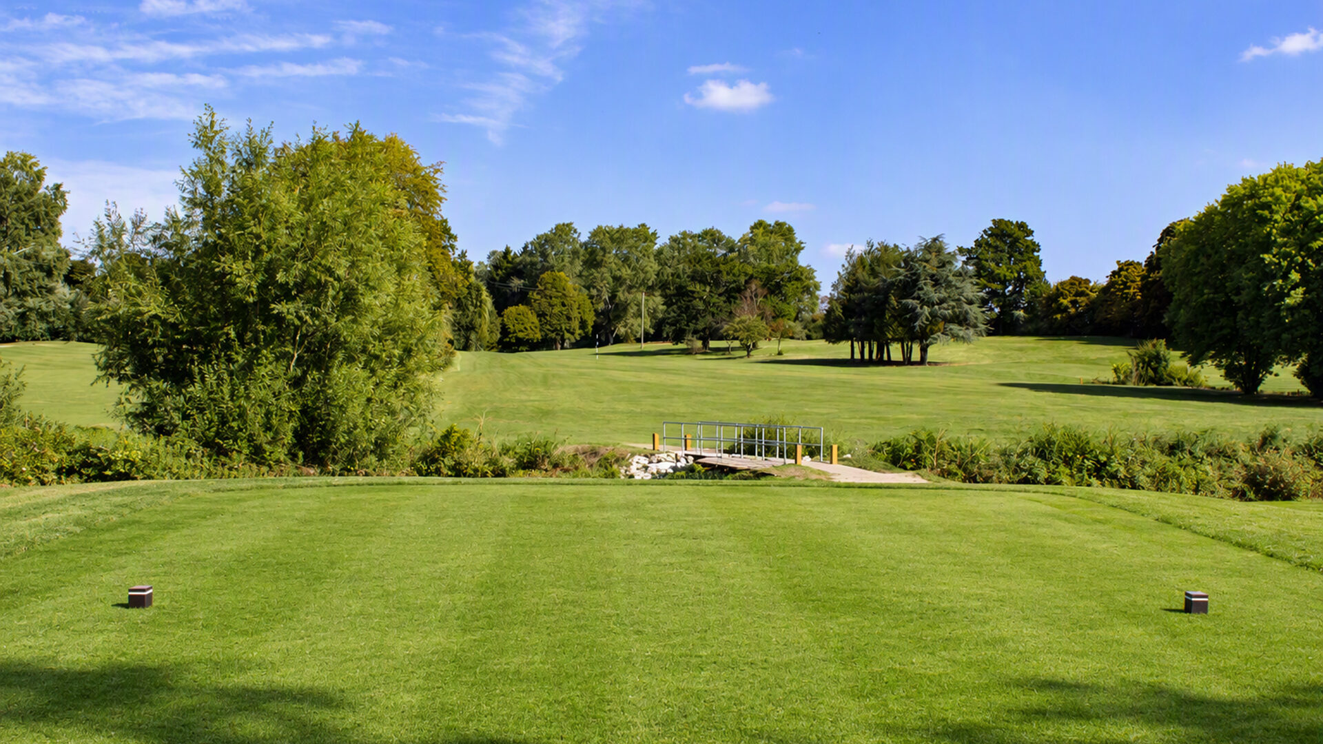 Golf course tee box with a view of the fairway and a small bridge.