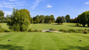 Golf course tee box with a view of the fairway and a small bridge.