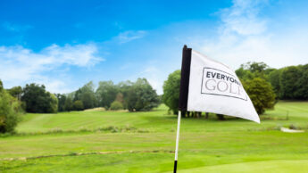 A golf flag with "Everyone Golf" text on a green course under a blue sky.