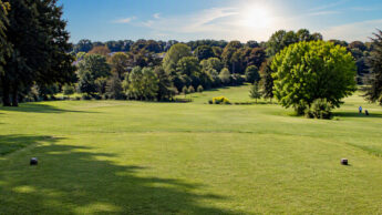 A scenic view looking down a green golf course fairway toward a tree-lined horizon.