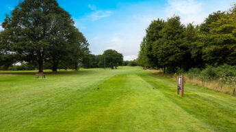 Golf course fairway with green grass, trees, and a blue sky on a clear day.