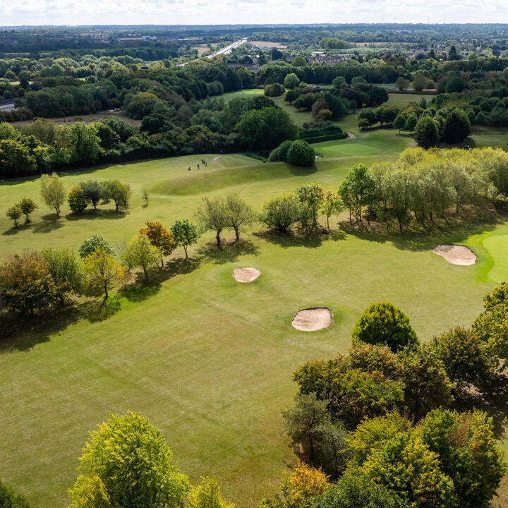 Aerial view of a Enderby golf course with sand bunkers, trees, and distant greenery.