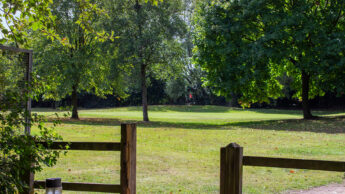 View of a green at Enderby golf course with trees, grass, and a red flag in the distance.
