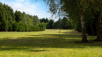 Large Enderby Golf Course with tall trees, two people playing golf under a blue sky.
