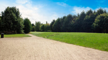 A path curves through Enderby Golf Course with trees under a blue sky.