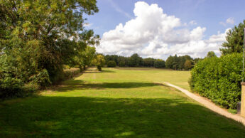 Grassy golf course tee with trees on both sides under a bright blue sky with some clouds.