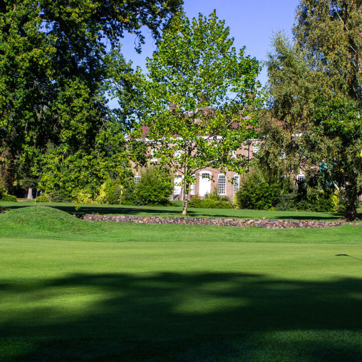 Batchwood Hall with white windows, surrounded by trees and a wide putting green.