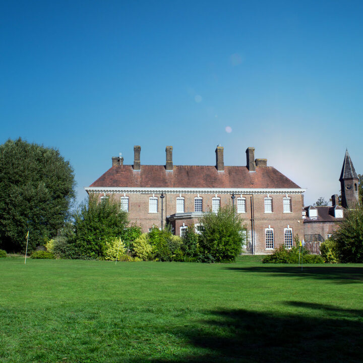 Batchwood Hall with white windows, surrounded by trees and a wide putting green.