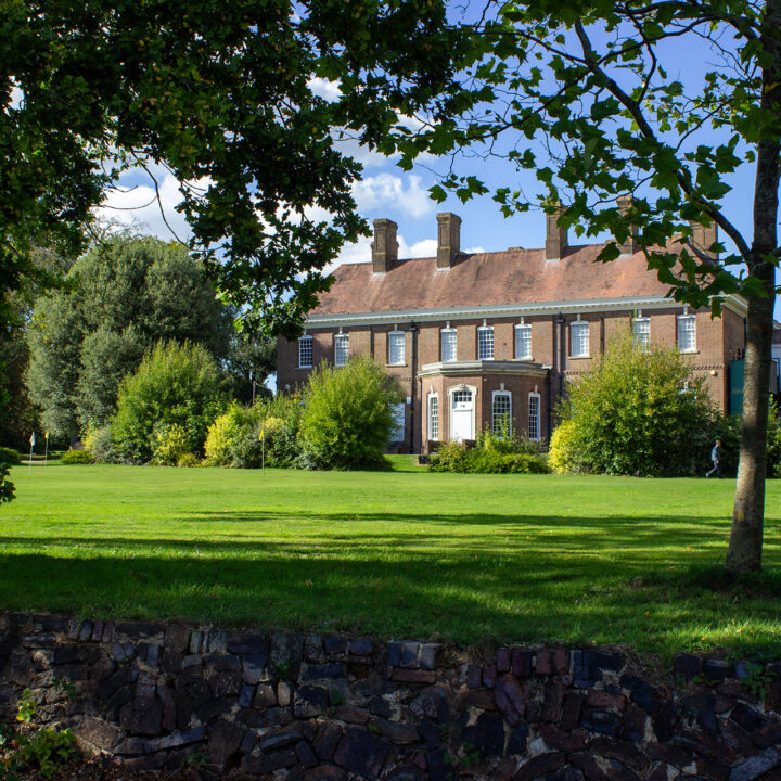 Batchwood Hall with white windows, surrounded by trees and a wide putting green.