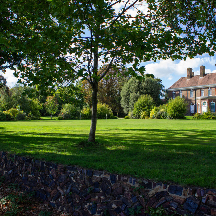 Batchwood Hall with white windows, surrounded by trees and a wide putting green.