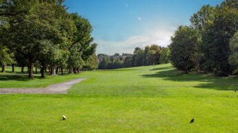 Sunny day at a golf course with green grass and trees lining the fairway.