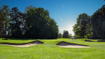 Golf course with sand bunkers, green grass, and trees under a bright blue sky.
