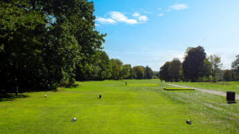 A sunny golf course with green grass, trees, and a clear blue sky.
