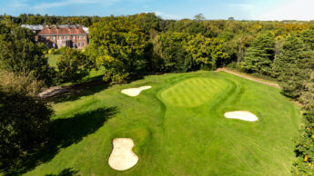 A golf course with a large green field and trees.
