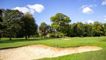 A sand trap on a golf course surrounded by green grass and trees under a blue sky.