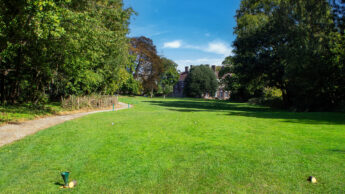 A golf course tee box with trees and a building in the background under a blue sky.