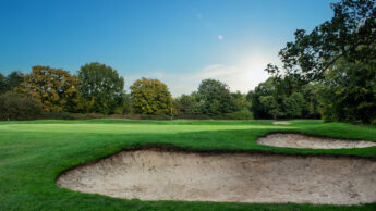 A golf course with sand bunkers, green grass, and trees under a clear blue sky.